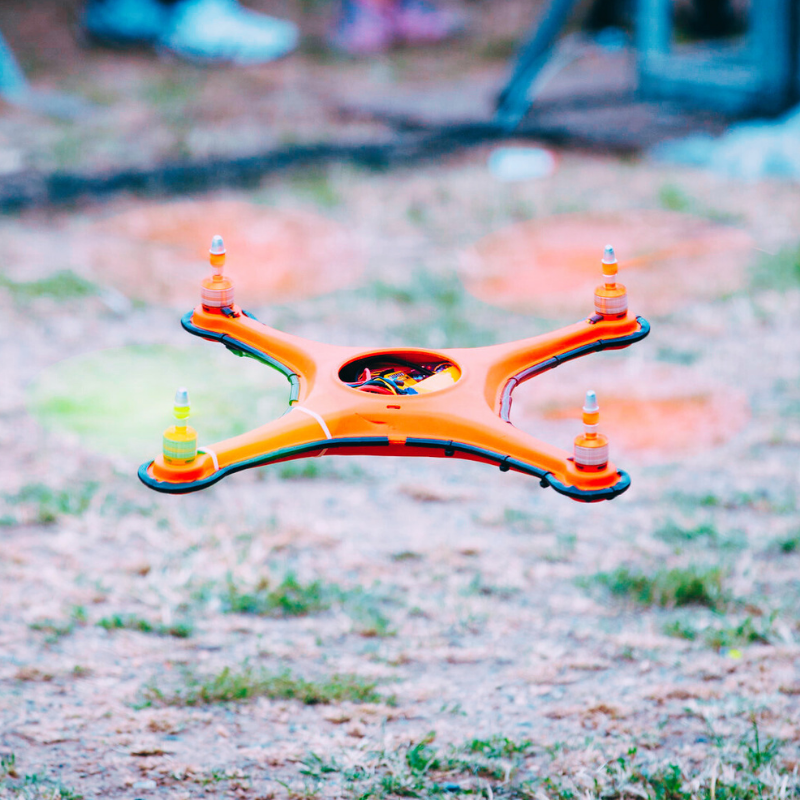 A vibrant orange drone hovering above the ground, representing our Drones & Flight collection for enthusiasts.