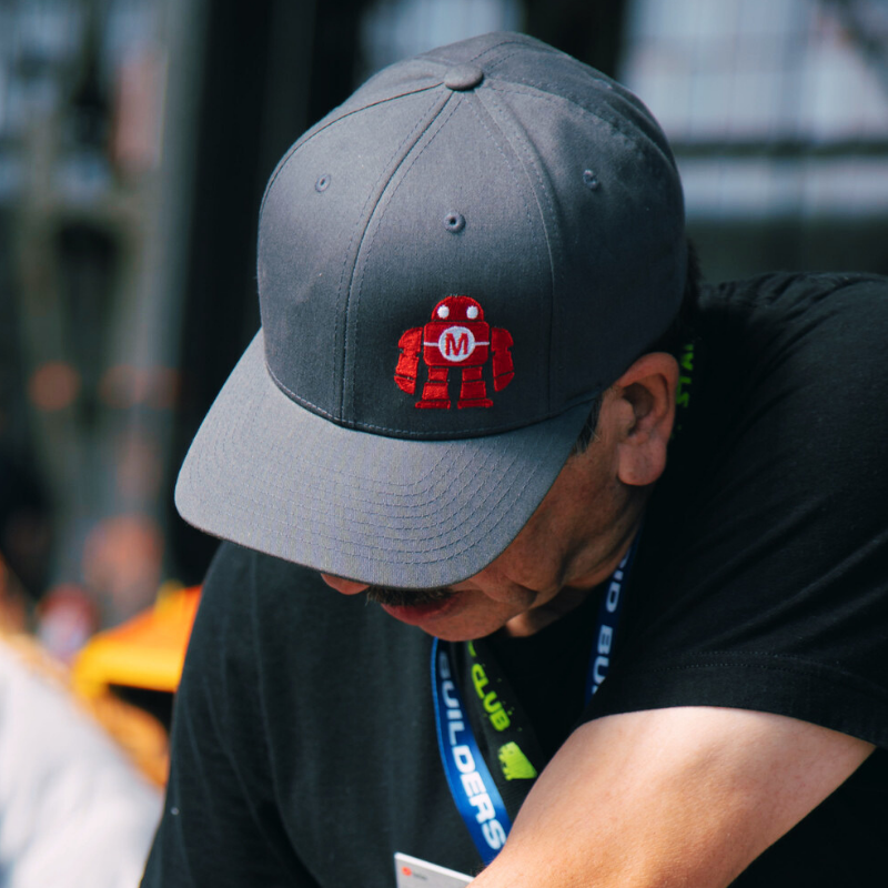 Person wearing a gray hat with a red robot logo, showcasing style from the Hats and Beanies collection.