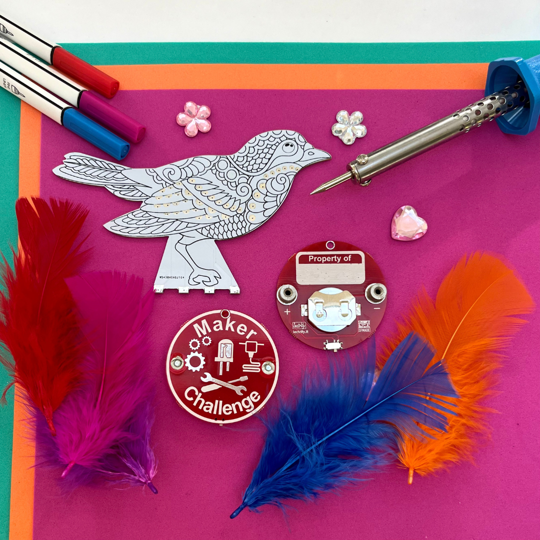 Craft materials for the Blinker Bird soldering kit, featuring feathers, a circuit board, and colorful markers.