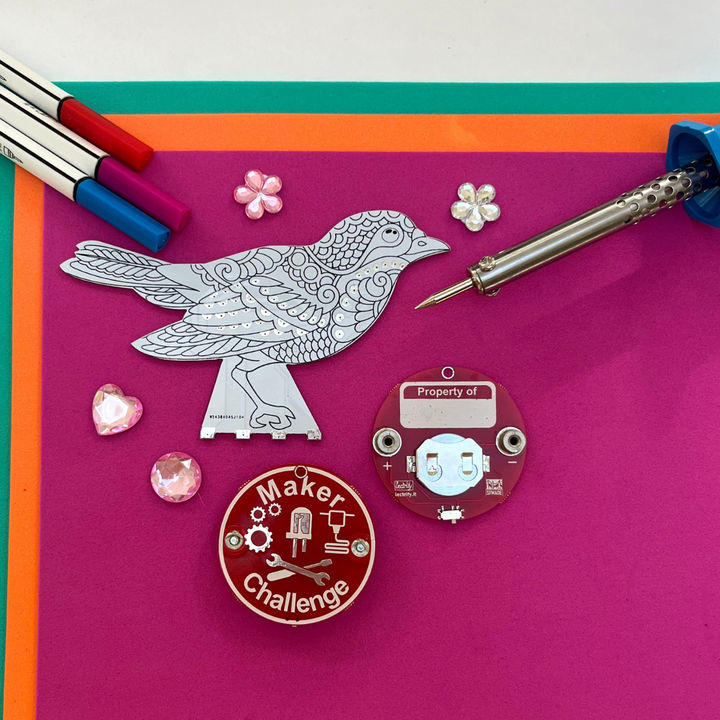 Blinker Bird soldering kit components including LED, circuit board, and decoration items on colorful background.