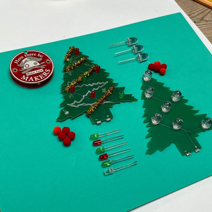 Learn To Solder - Holiday Tree kit with LED components and personalizing materials on a teal background.