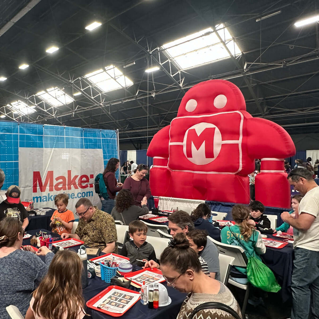 Maker Faire event with people around tables, a large inflatable Makey robot with &