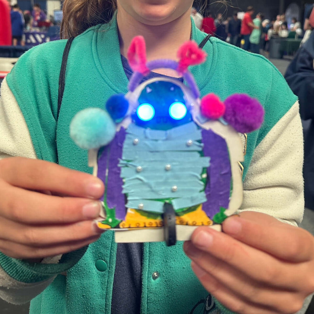 Person holding a colorful craft project with lights and pom-poms