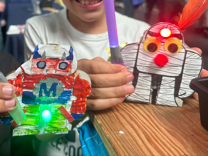 Two children holding colorful crafts at a craft-making Make: event.