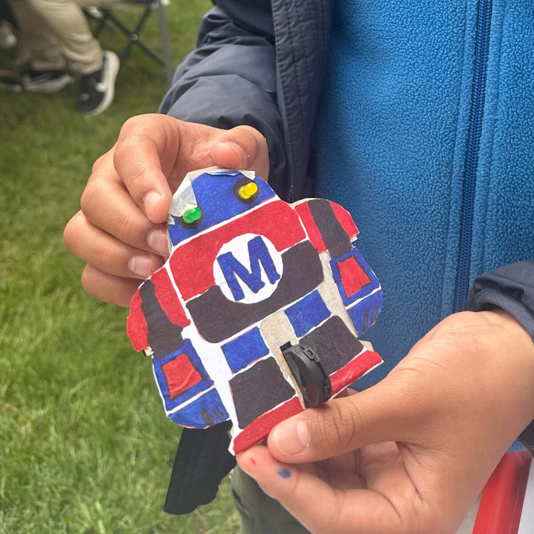 Child holding a colorful LED cardboard project outdoors at Maker Faire