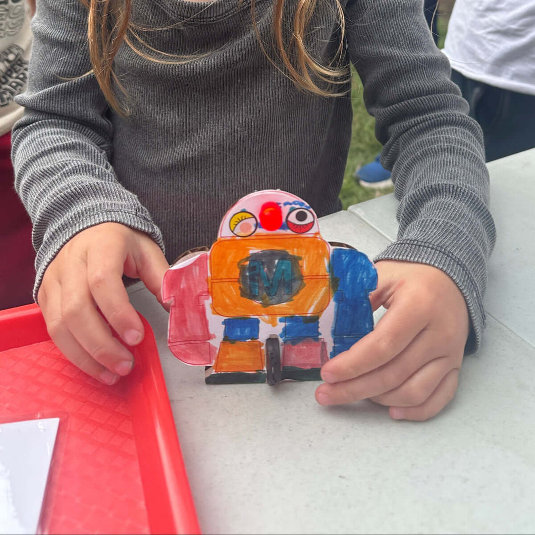 Child holding a colorful cardboard project at Maker Faire