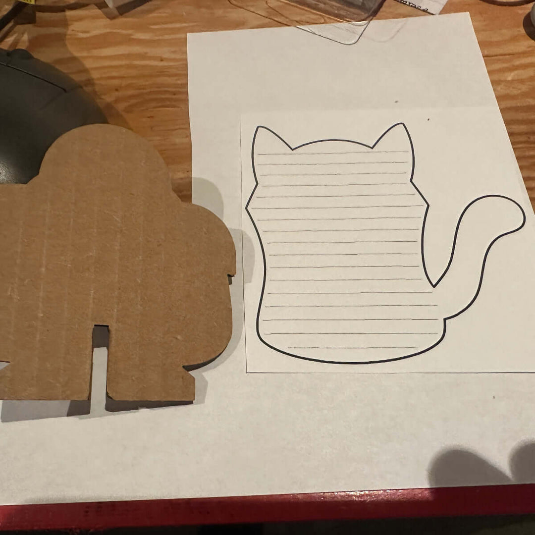 Cardboard cutout with a cat shape paper template on a wooden surface.