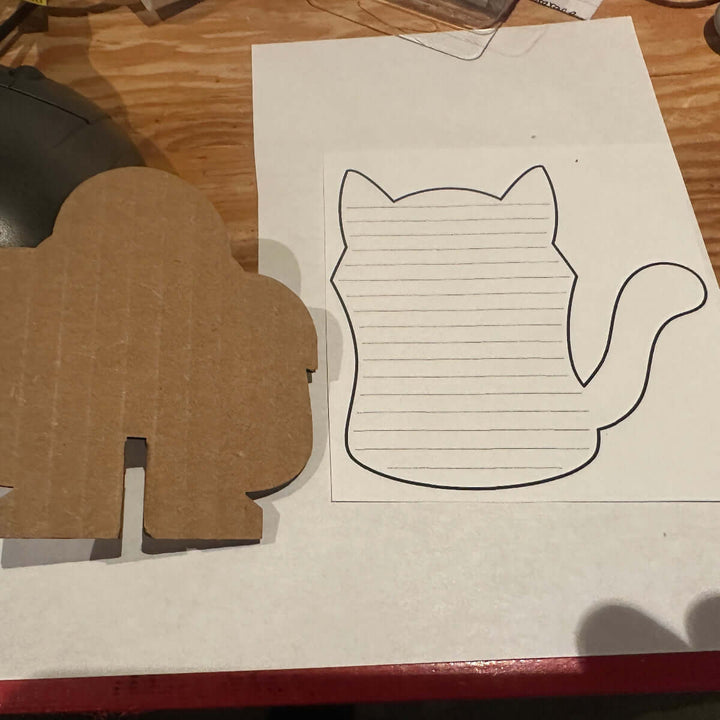 Cardboard cutout with a cat shape paper template on a wooden surface.
