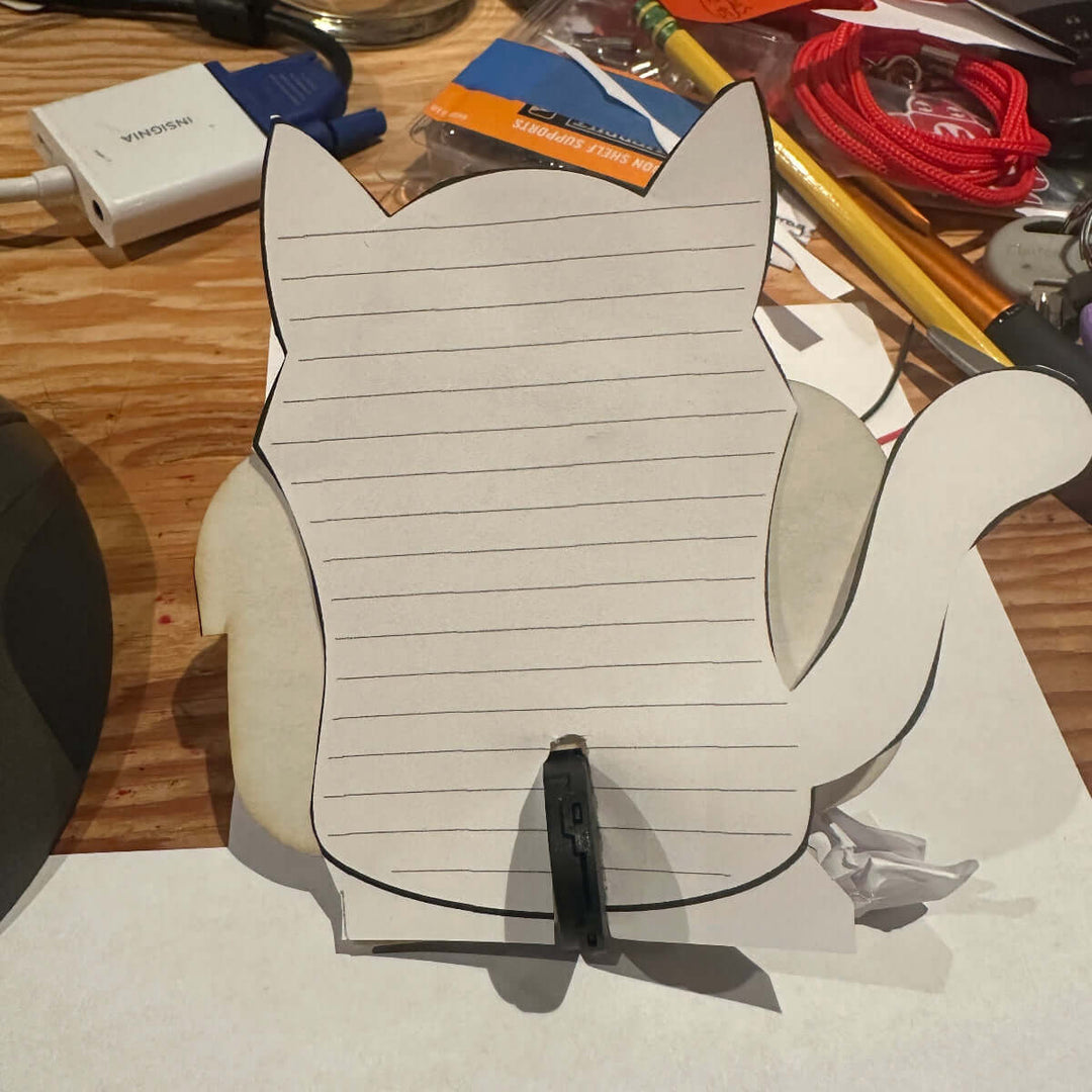Cardboard cutout with a cat template attached on a cluttered desk