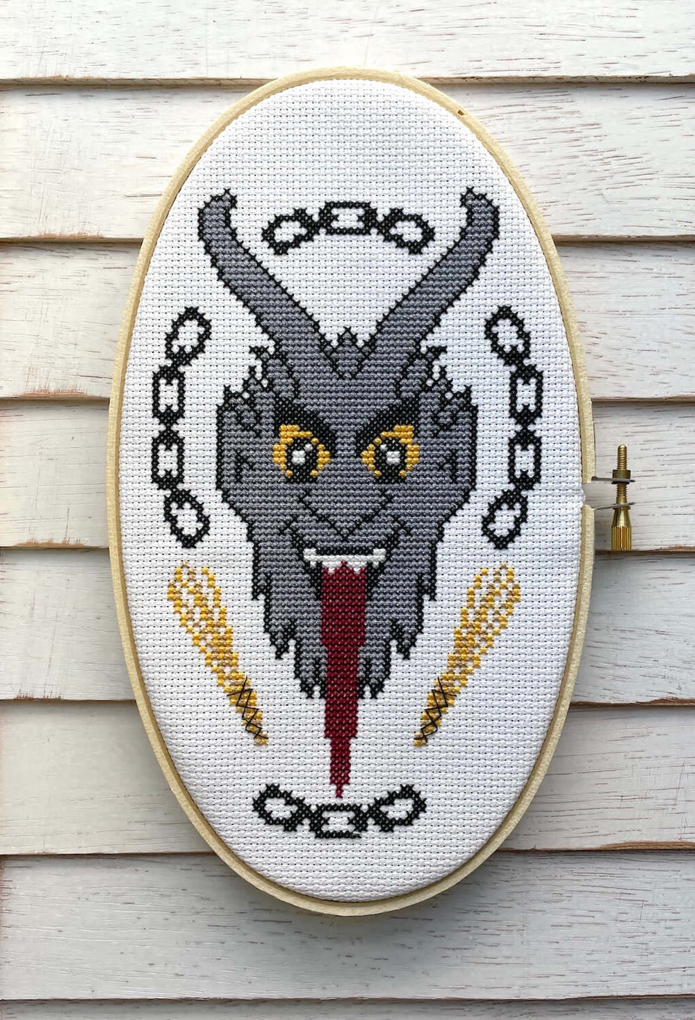 The Krampus Counted Cross Stitch DIY Kit finished design featuring a menacing Krampus portrait with chains and a tongue.