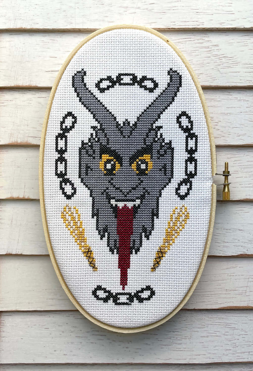 The Krampus Counted Cross Stitch DIY Kit finished design featuring a menacing Krampus portrait with chains and a tongue.