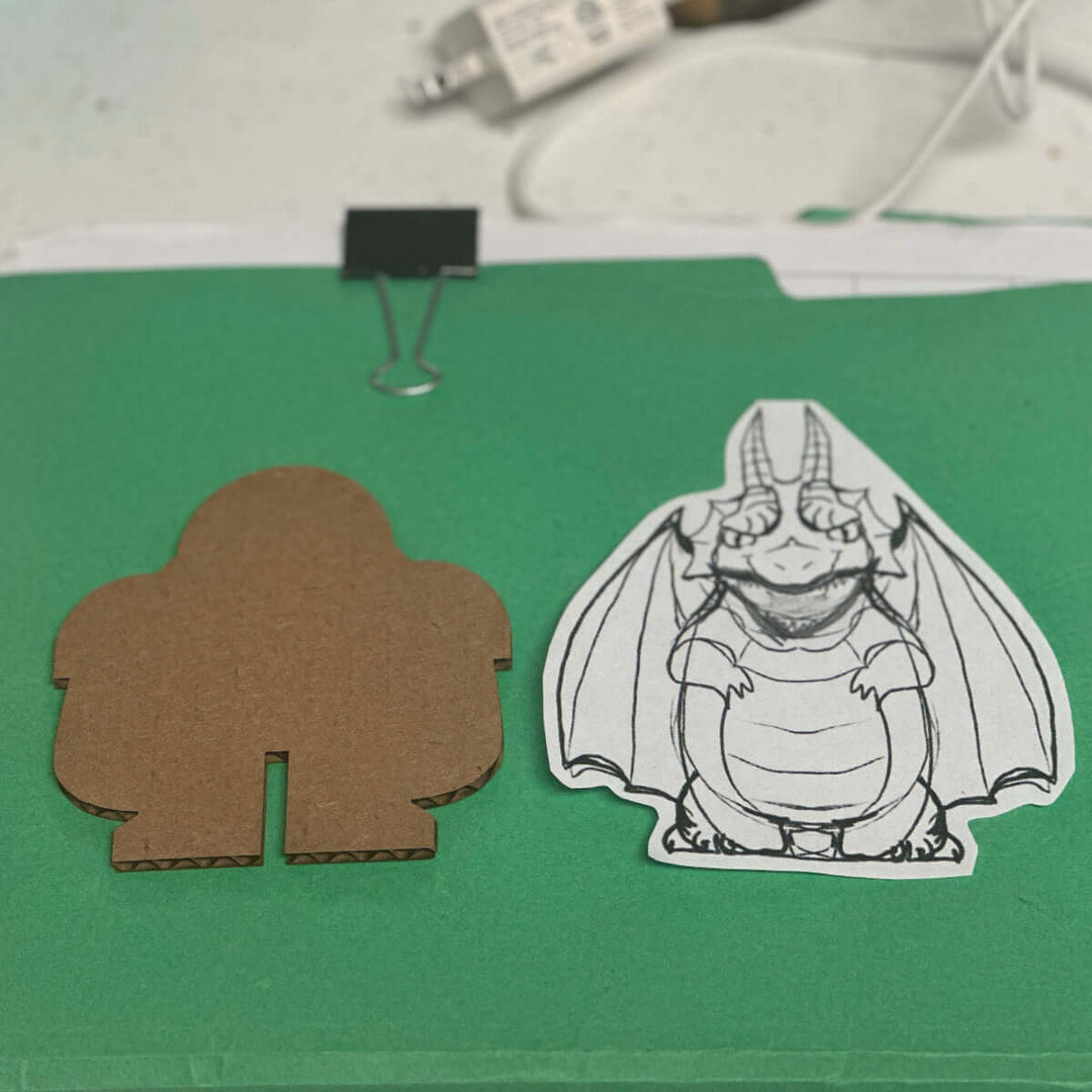 Cardboard cutout with a dragon character template on a green surface.