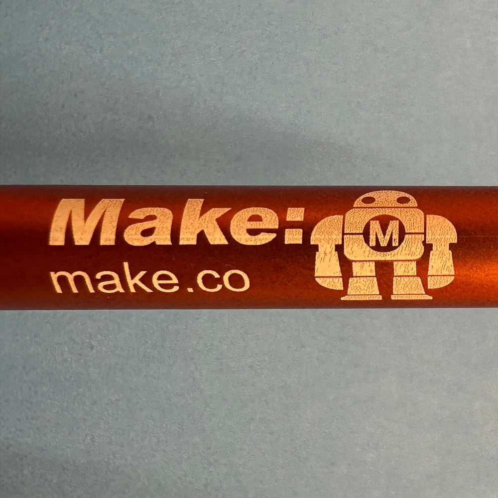 Orange pen with Makey the robot and 'make.co' branding on a gray background