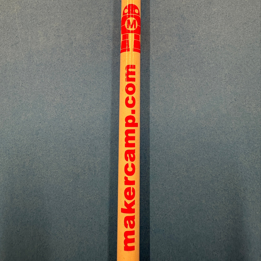 Pencil with a red Makey robot logo and makercamp.com print lying on a gray background