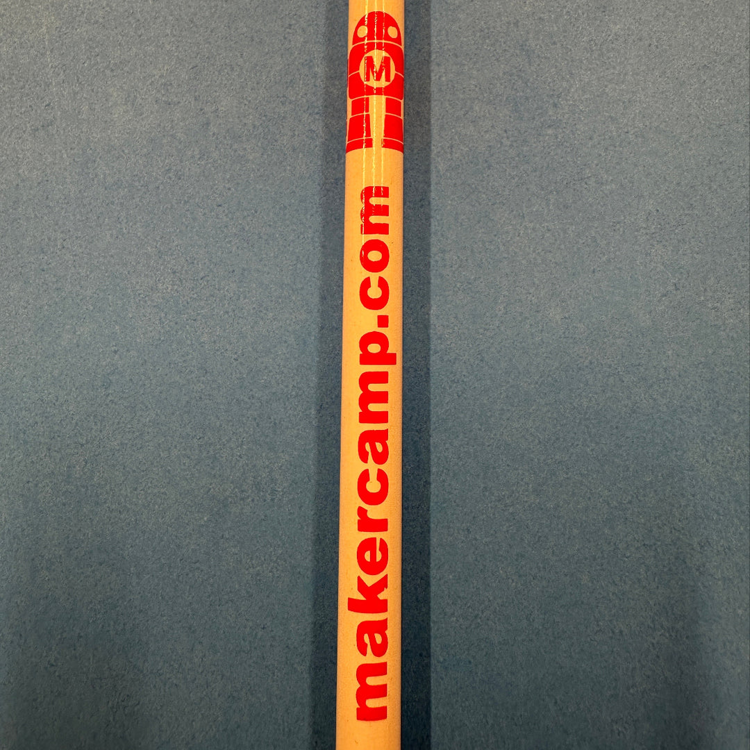 Pencil with a red Makey robot logo and makercamp.com print lying on a gray background
