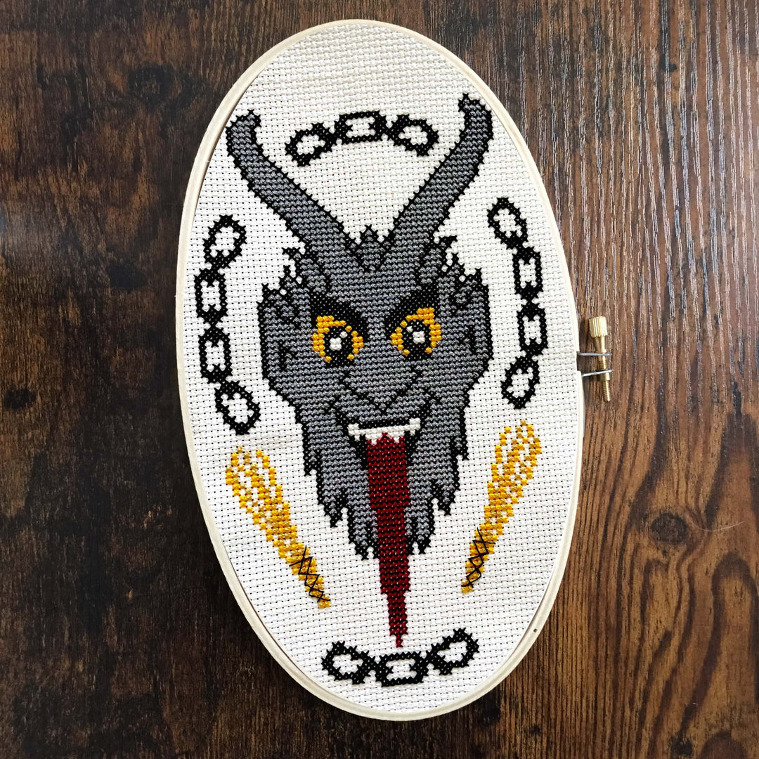 The Krampus Counted Cross Stitch DIY Kit finished design featuring a menacing Krampus portrait with chains.