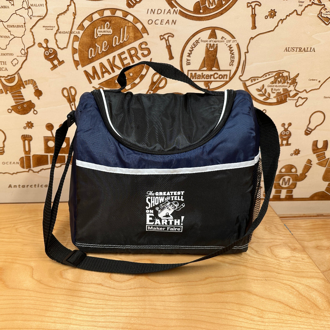Navy blue cooler bag with white Maker Faire branding on a wooden surface with a map-themed background