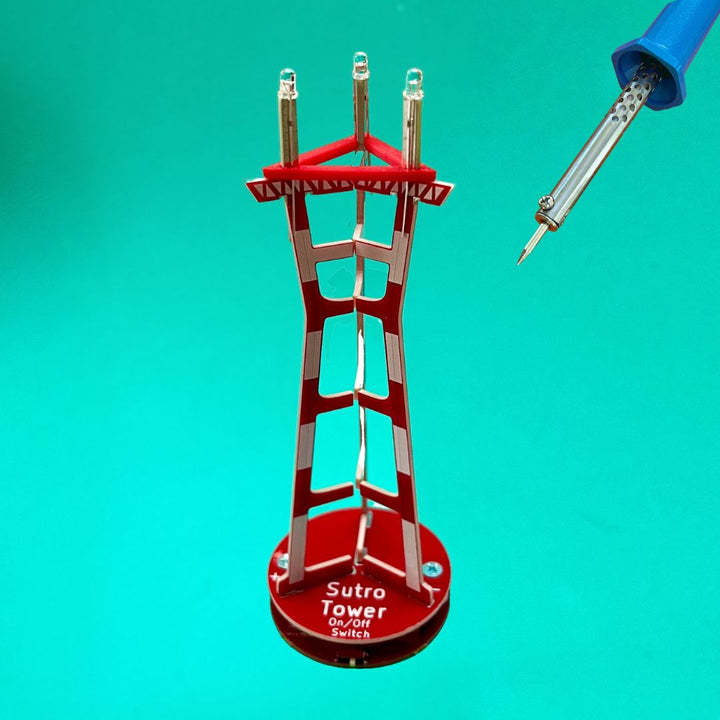Soldering Kit: Sutro Tower model with LED lights and soldering iron against a teal background.